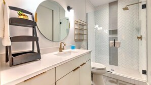Een moderne badkamer met een wit wastafelmeubel, gouden details, een grote spiegel en een douche met een visgraatmozaïek.