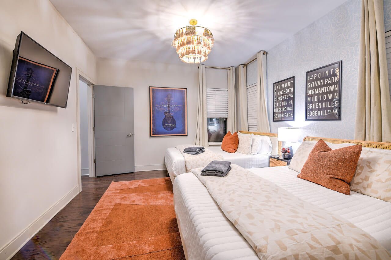 A hotel room with a large bed, a chandelier, a flat-screen TV, and framed artwork on the walls.