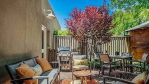 Eine Terrasse mit Gartenmöbeln, einem Grill und einem Baum mit roten Blättern.