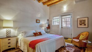 Ein Schlafzimmer mit Bett, Nachttisch, Lampe, Gitarre, Stuhl und einer Tür mit Fenster.