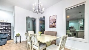 A dining area with a wooden table, four chairs, a chandelier, a bookshelf, and a large window. - Huge Lux Home Rooftop Views + Hot Tub, Pool+Sauna! (Nashville)