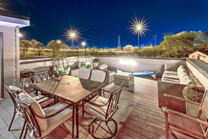 An outdoor patio with a dining table and chairs, a seating area with cushions, and a view of the surrounding landscape.