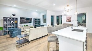 A modern kitchen with a central island, built-in shelving, and a dining area with a sofa and chairs. - Huge Lux Home Rooftop Views + Hot Tub, Pool+Sauna! (Nashville)