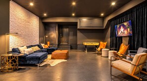 Ein modernes Wohnzimmer mit Backsteinwand, dunklen Sofas, einem Kicker und einem Flachbildfernseher.