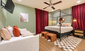 Une chambre à coucher avec un lit à baldaquin, un bureau avec une chaise, un téléviseur fixé au mur et un ventilateur de plafond.