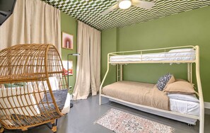 Ein Stockbett mit Kopfteil, ein Korbstuhl, eine Stehlampe und ein gemustertes Teppich.