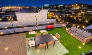 Eine Dachterrasse mit Tisch, Stühlen, einer Couch und Lichterketten.