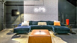 Un salon moderne avec un canapé d’angle, un pouf en cuir et un mur en briques agrémenté d’un néon.