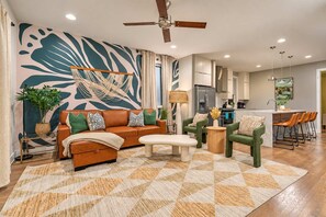 Ein modernes Wohnzimmer mit einer Couch, Sesseln, einem Couchtisch und einer Küche im Hintergrund.