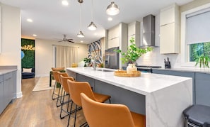 Une cuisine moderne dotée d’un îlot central, de tabourets de bar et de luminaires suspendus.