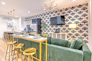 A modern kitchen with a bar area, green upholstered sofa, and a patterned wall.