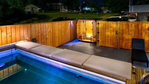 A hot tub with wooden walls and a built-in bench, surrounded by a pool.