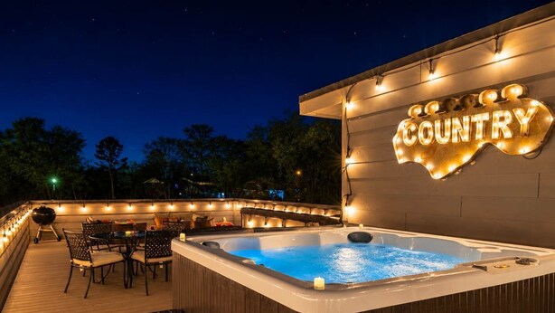 A hot tub on a wooden deck with string lights, a sign reading 'Country,' and outdoor furniture.