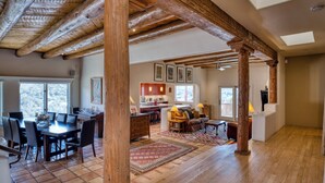 A spacious living area with a wooden ceiling, a dining table, and a kitchen in the background. - Casa San Miguel | Santa Fe Sanctuary with Views (Santa Fe)