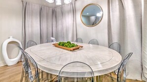 Ein runder Esstisch mit sechs Stühlen, eine Chandelier, ein runder Spiegel und eine weiße Toilette im Hintergrund.
