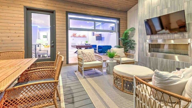 A cozy indoor space with wicker furniture, a flat-screen TV, and a large window. - Lux Home • 13 Beds • Walk 2 Restaurants • Rooftop (Berry Hill)