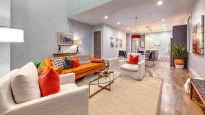 A modern living room with a sofa, armchairs, and a coffee table. There is a kitchen area with a sink and a dining table in the background. - Lux Home • 13 Beds • Walk 2 Restaurants • Rooftop (Berry Hill)