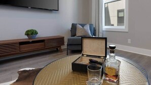 Un soggiorno con un tavolino in vetro, un telecomando, un bicchiere e una bottiglia di liquore.