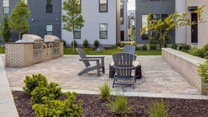 Una moderna area patio esterna con una griglia, due poltrone Adirondack e un tavolino.