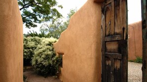 Een smal pad dat leidt naar een houten deur in landelijke stijl, omgeven door beige muren en groen.