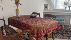A dining area with a round table covered by a patterned tablecloth, a wooden bench with a colorful cushion, and a vase with dried flowers. - Charming Apartment in the Heart of Paris. Families are Welcome (Paris)