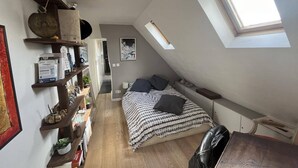 A small, cozy attic bedroom with a sloped ceiling, a skylight, a bed with patterned bedding, and shelves with various items. - Charming Apartment in the Heart of Paris. Families are Welcome (Paris)