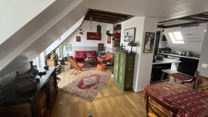 A loft-style apartment with a high ceiling, exposed beams, a dining area with a table and chairs, a kitchen area, and a cozy seating area with a sofa and armchairs. - Charming Apartment in the Heart of Paris. Families are Welcome (Paris)