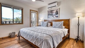 Ein Schlafzimmer mit einem hölzernen Bett, einem Deckenventilator, einer Klimaanlage, einem Fenster mit Blick und einer Stehlampe.