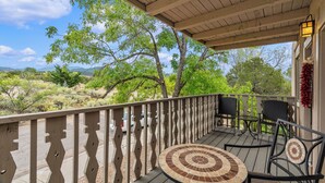 Eine Holzterrasse mit rundem Tisch und Stühlen, mit Blick auf eine malerische Landschaft aus Bäumen und Hügeln.