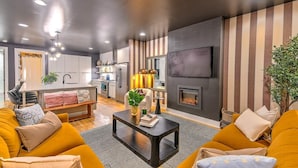 Ein modernes Wohnzimmer mit Sofa, Couchtisch und Kamin. Es gibt eine Küchenzeile mit Schränken und einem Esstisch.