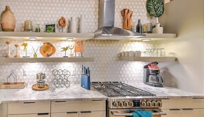 A modern kitchen with a gas stove, oven, and various kitchenware on shelves.