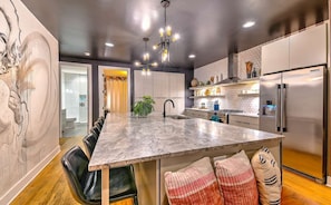 A modern kitchen with a marble island, stainless steel appliances, and a pendant light.