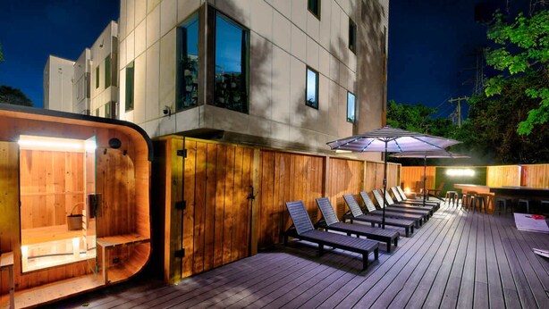 Terraza de madera con sillones de descanso y zona de sauna contigua a un edificio moderno.