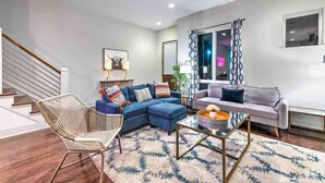A modern living room with a sectional sofa, a coffee table, and a wicker chair. - Premiere Gulch Home, 15 Beds! Best Skyline Views! (Nashville)