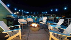 A rooftop deck with a fire pit, lounge chairs, and city lights in the background. - Premiere Gulch Home, 15 Beds! Best Skyline Views! (Nashville)
