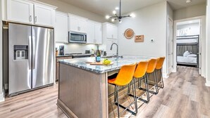 A modern kitchen with white cabinets, a stainless steel refrigerator, a microwave, and a bar area with orange chairs. - Huge Downtown Luxury Home Rooftop Deck 12 Beds (Nashville)