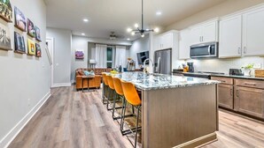 A modern kitchen with a central island, bar stools, and a dining area with a sofa. - Huge Downtown Luxury Home Rooftop Deck 12 Beds (Nashville)