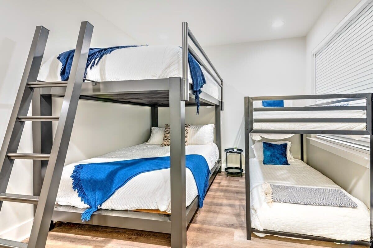 Une chambre avec un lit superposé, une petite table de chevet et une fenêtre avec des stores.