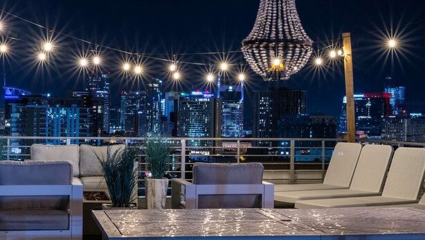 A rooftop lounge with a city skyline view, string lights, and a decorative chandelier. - Rooftop Pool Table Gulch! City Views! 15 beds! (Nashville)