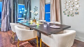 A dining room with a long table, white chairs, and a modern chandelier. - Rooftop Pool Table Gulch! City Views! 15 beds! (Nashville)