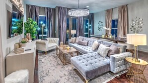 A spacious living room with a grey sofa, a white armchair, and a coffee table. There is a chandelier, a plant, and a lamp on a side table. - Rooftop Pool Table Gulch! City Views! 15 beds! (Nashville)