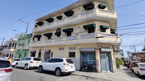Un edificio de varios pisos con balcones, un cartel que dice "TIEMPO" y coches estacionados en la calle.