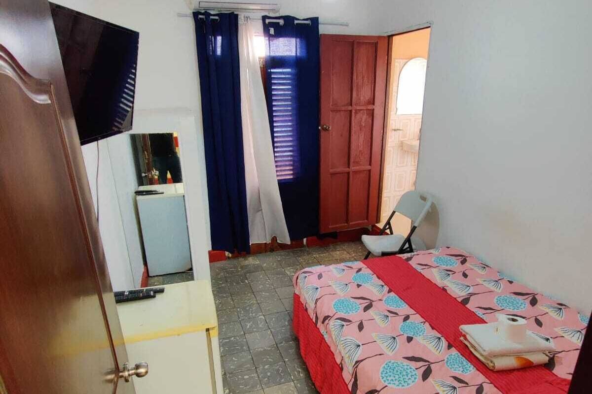 A bedroom with a bed, a desk, a chair, a television, and a window with curtains.