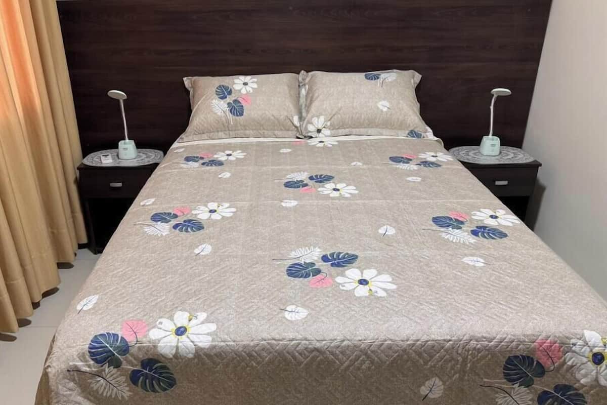 A bed with a floral bedspread, two bedside tables with lamps, and a curtain.