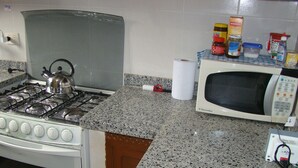A kitchen with a gas stove, a microwave, and various kitchen items on the counter. - Surbackpackers (Santa Cruz)