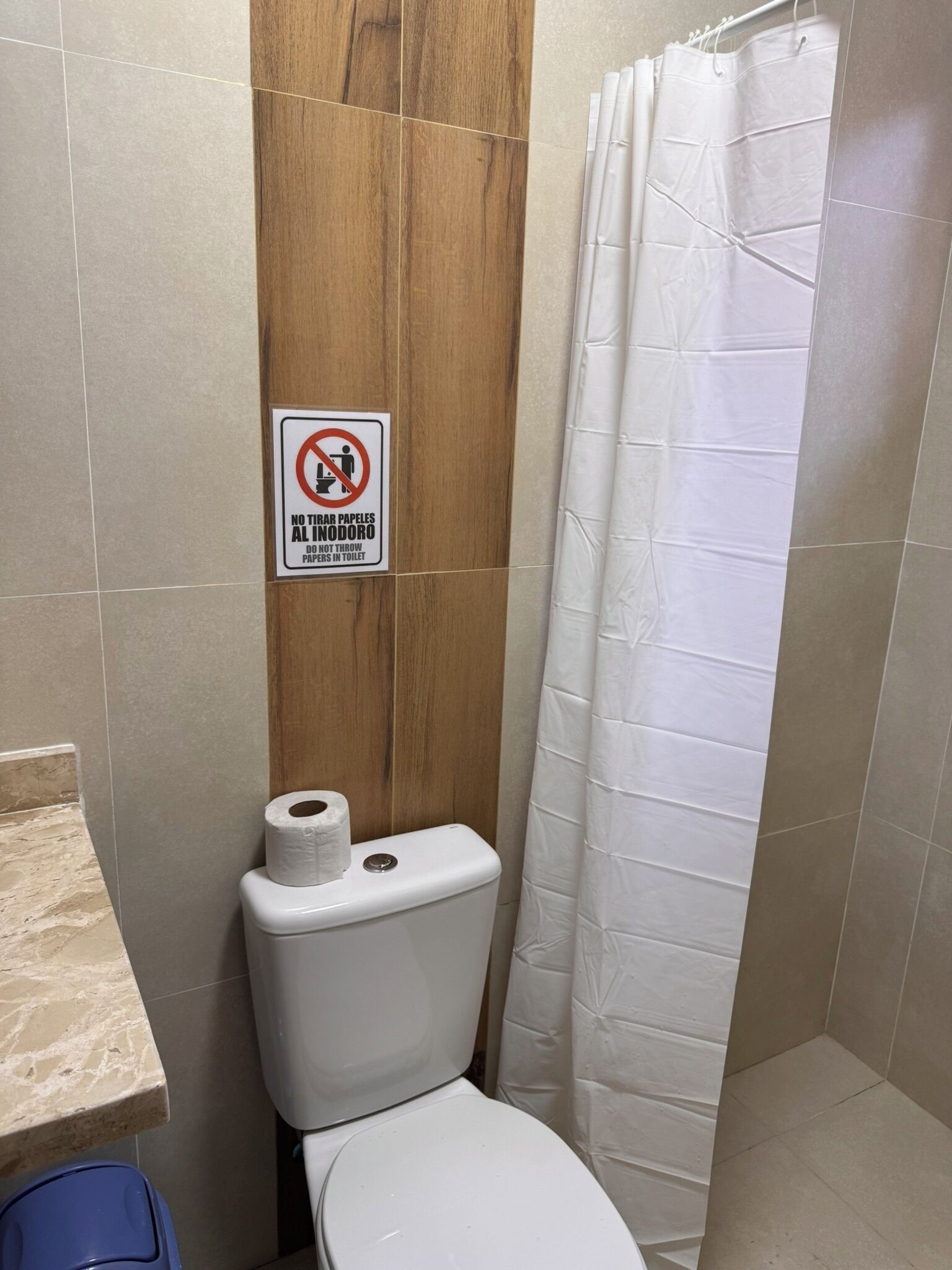 A bathroom with a toilet, a shower curtain, and a sign prohibiting the disposal of paper products in the toilet.