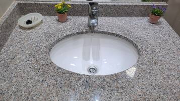 A bathroom sink with granite countertop, a mirror, and two potted plants.