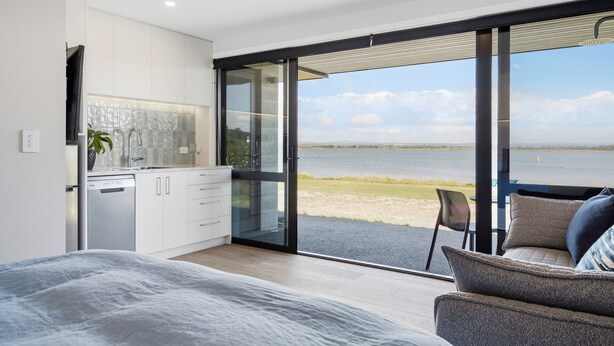 Une chambre moderne avec un grand lit, une vue sur un lac et une porte-fenêtre coulissante donnant sur un balcon.