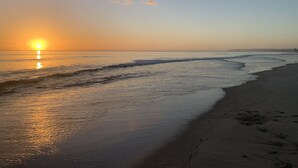 Une plage au coucher du soleil, où les vagues viennent doucement lécher le rivage.