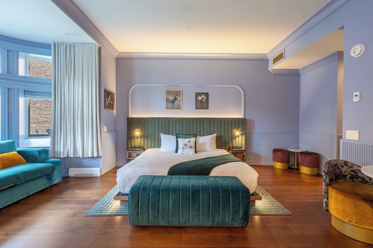 Quarto moderno com uma cama grande, um banco estofado verde, um sofá azul-turquesa e uma pequena mesa redonda.